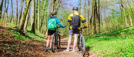 Dos ciclistas en un sendero forestal, rodeados de árboles y follaje.