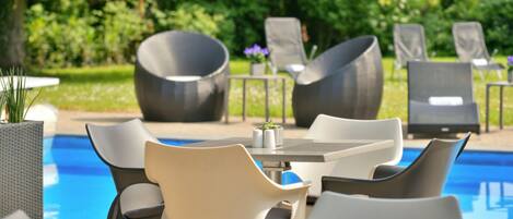 Un espace aménagé au bord de la piscine, avec des chaises longues et une table, le tout entouré de verdure.