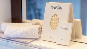 Une étagère en verre présente une sélection d’éponges et de serviettes de massage de la marque Babor.