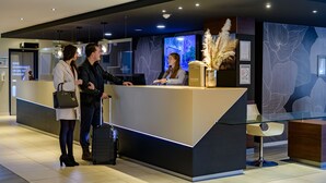 Un moderno mostrador de recepción con separador de vidrio, una pantalla digital y un jarrón decorativo con plumas de miscanthus.