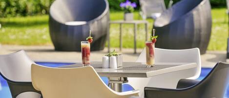 A poolside seating area with chairs and a table, two drinks with strawberries, and a small plant on the table.