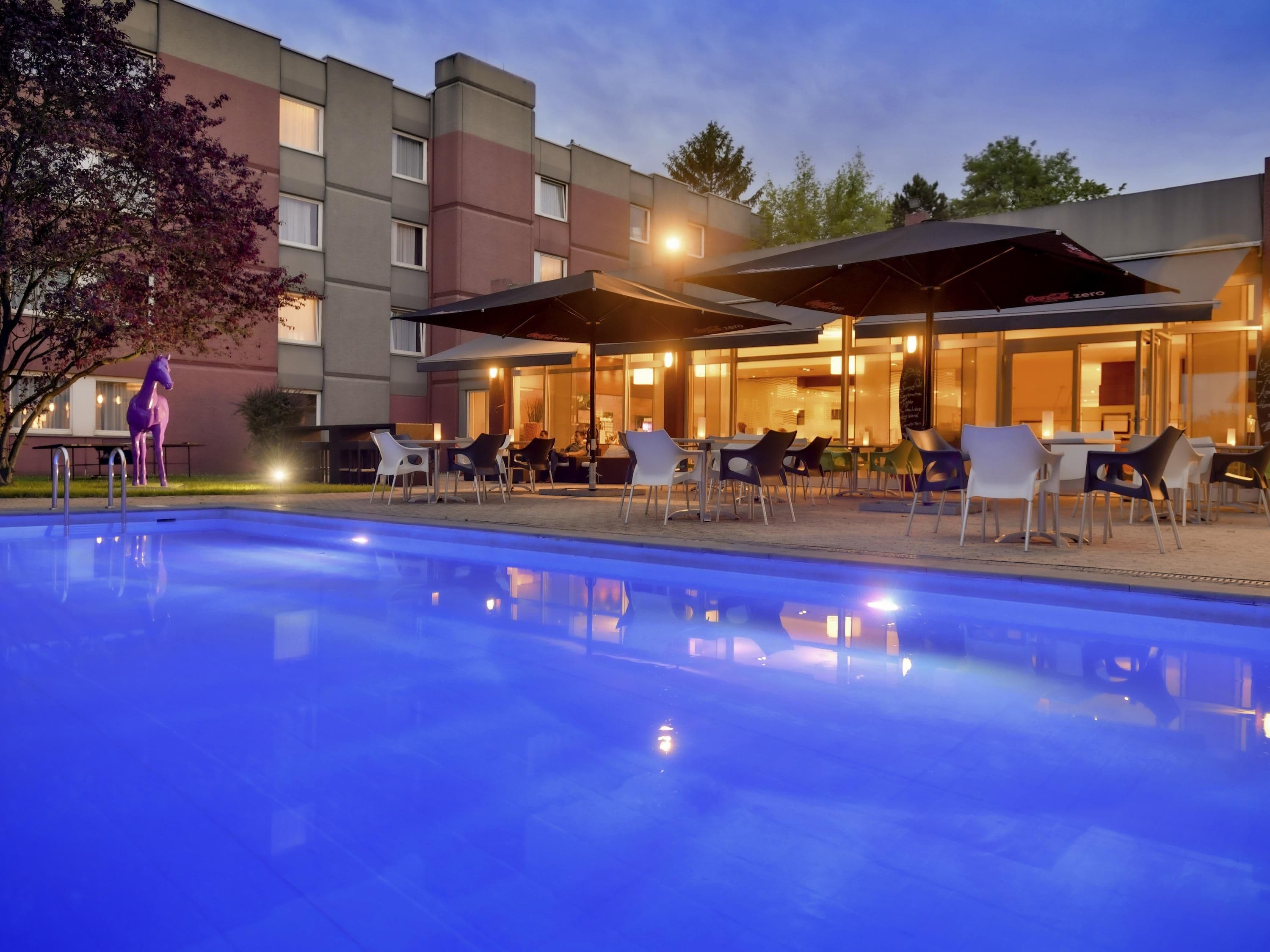 A poolside area with outdoor seating and umbrellas, a statue, and a building with multiple windows.
