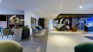 Eine moderne Hotellobby mit Empfangstresen, Sitzgelegenheiten und Zierpflanzen.