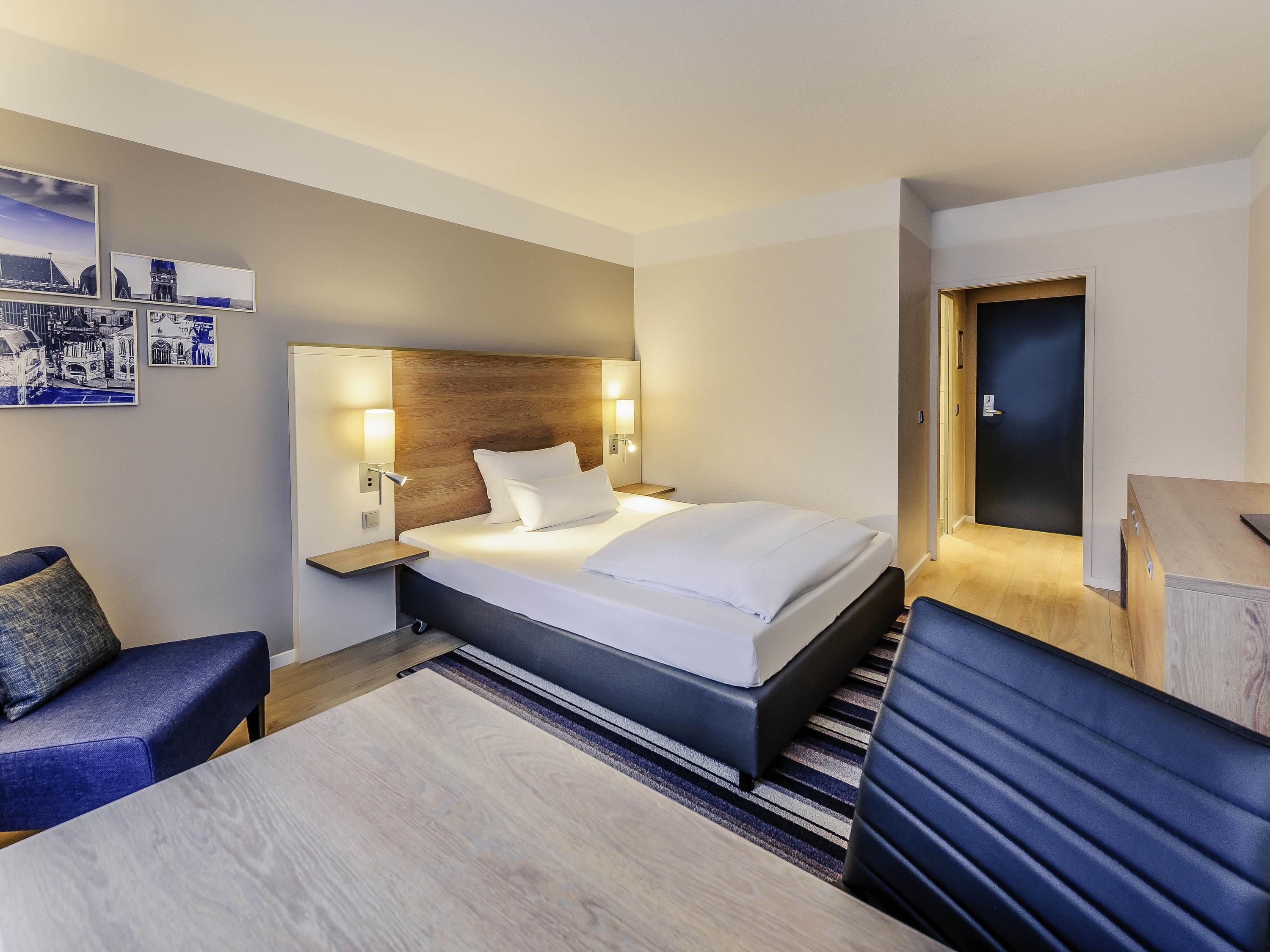 Una habitación de hotel con cama, mesitas de noche, escritorio, silla y puerta.