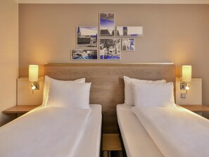 Une chambre d’hôtel avec deux lits, une tête de lit en bois, des cadres photos fixés au mur et des lampes de chevet.