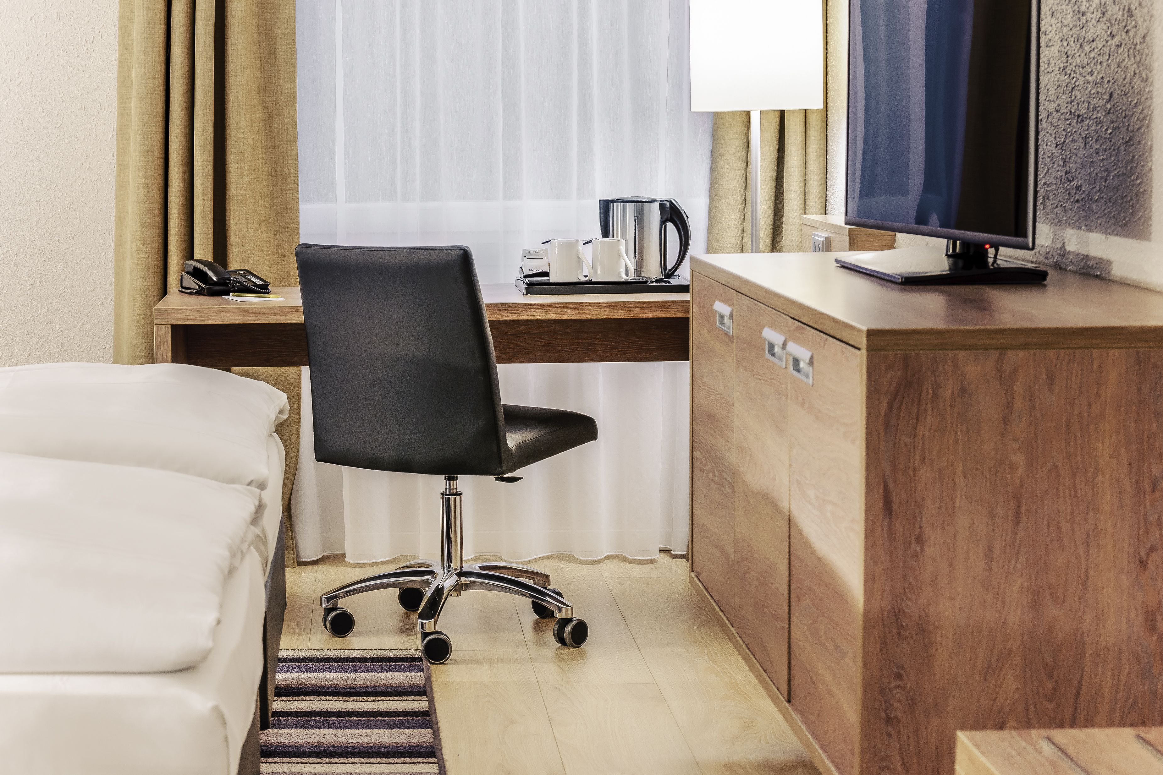 A hotel room with a bed, a desk with a computer, a chair, a coffee maker, and a television.