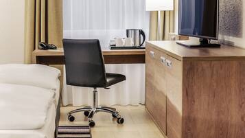 A hotel room with a bed, a desk with a computer, a chair, a coffee maker, and a television.