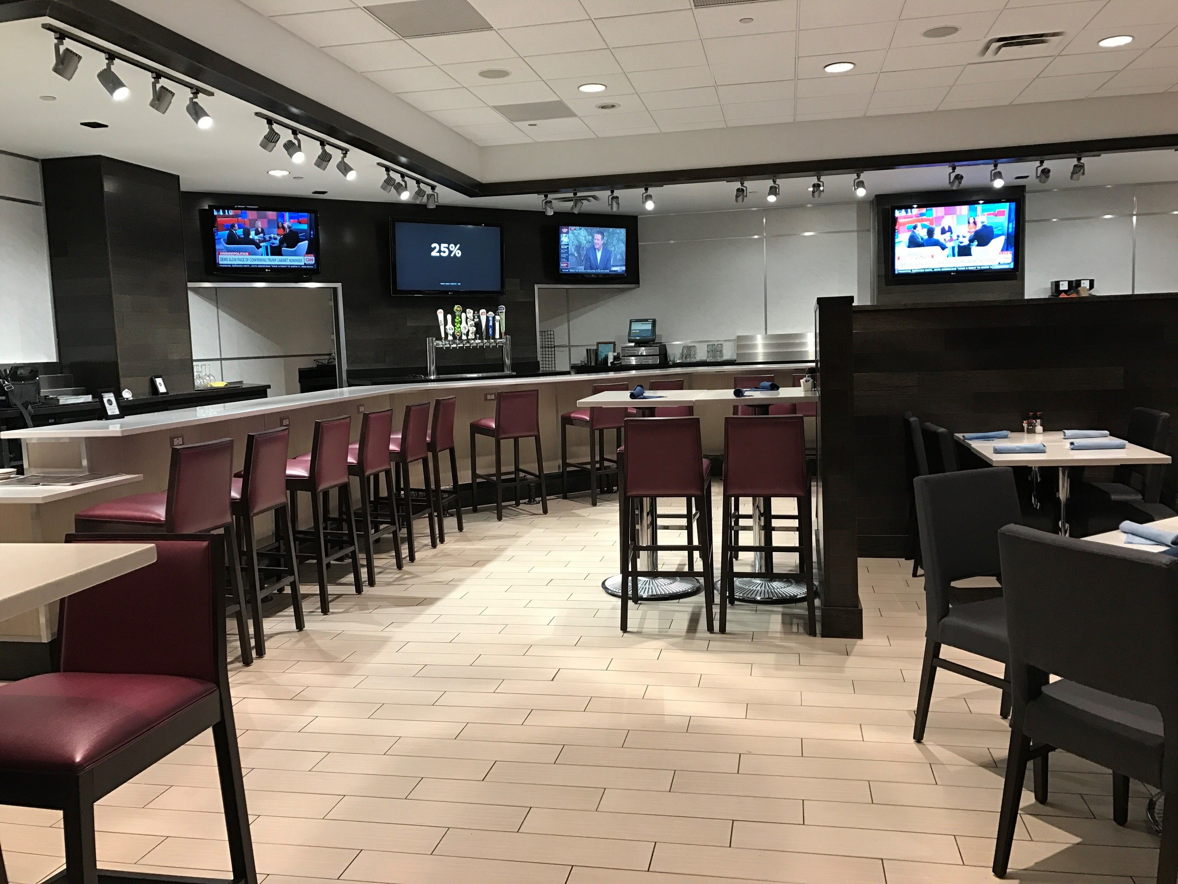 A modern restaurant with bar seating, multiple TVs, and a digital display showing '25%'.