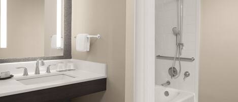 A modern bathroom with a white sink, two faucets, a mirror, and a shower with a handheld showerhead and a handheld shower attachment.