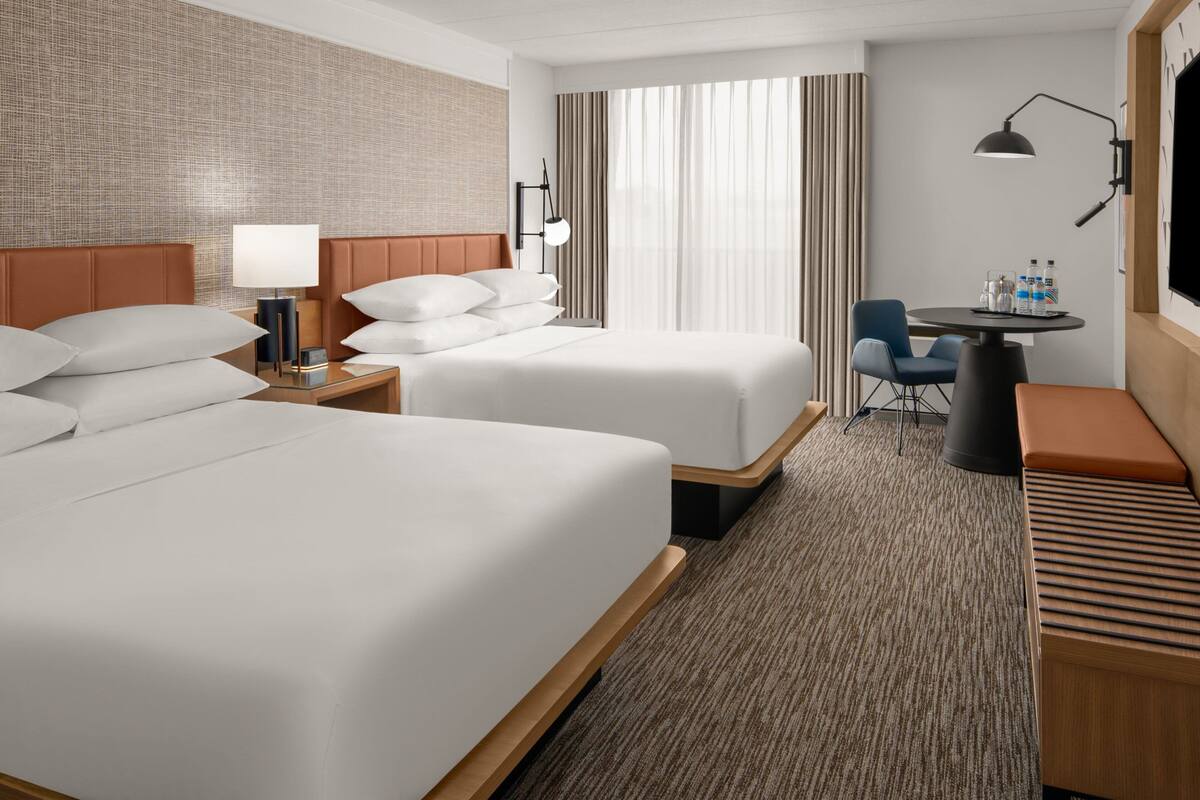 A hotel room with two beds, a desk with a chair, a TV, and a window with curtains.