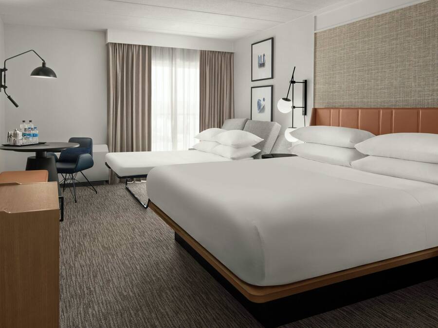 A hotel room with a large bed, a desk with a chair, a small table, and a TV.