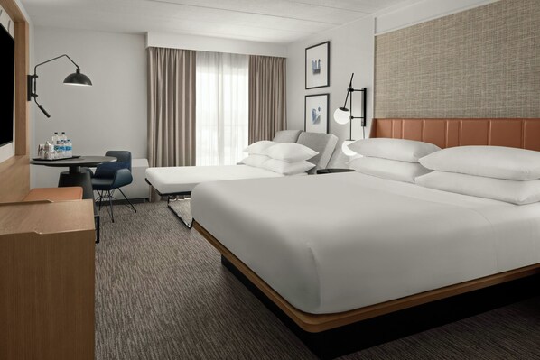 Habitación de hotel con una cama grande, un escritorio con una silla, una mesita pequeña y un televisor.
