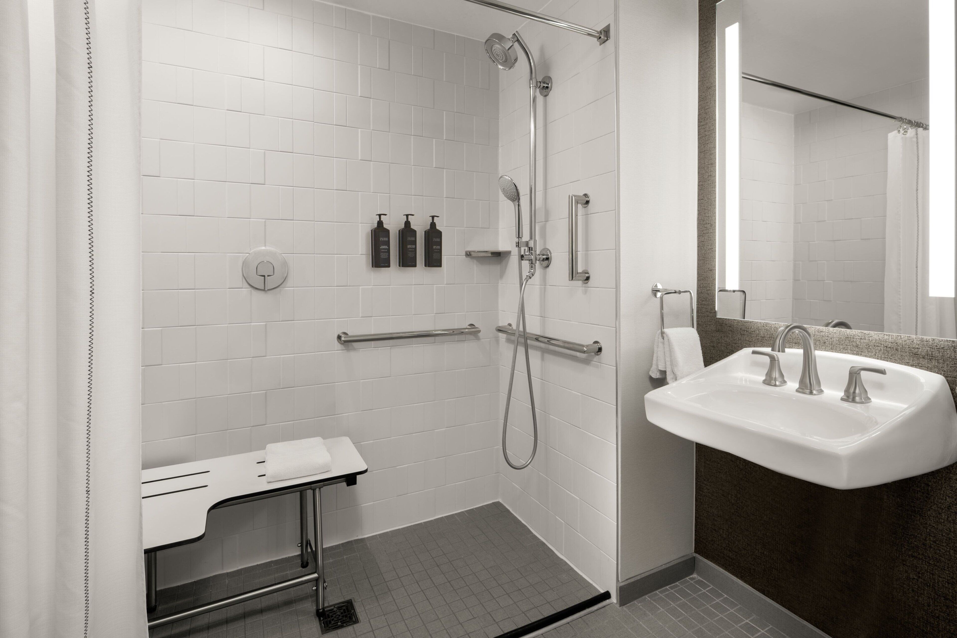 A modern bathroom with a walk-in shower, grab bars, a sink, and a mirror.