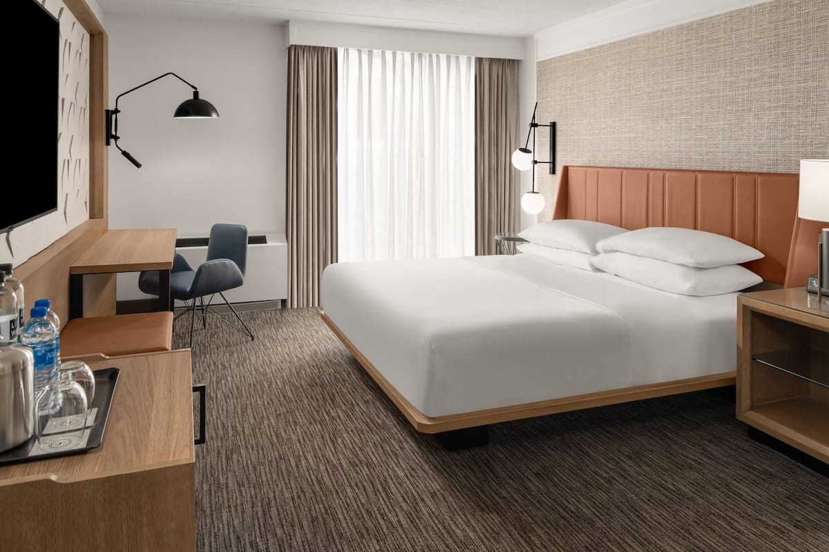 A hotel room with a large bed, a desk with a chair, a TV, and a minibar.