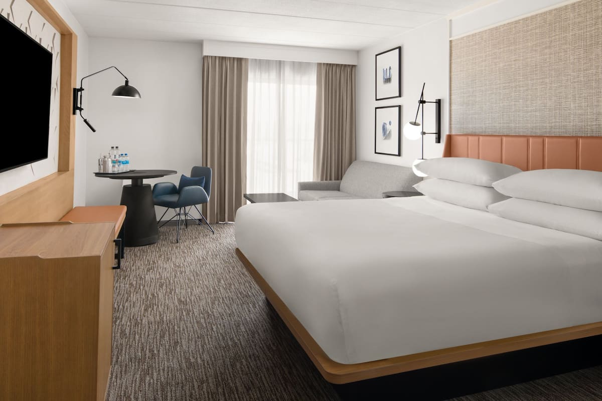 A hotel room with a large bed, a desk with a chair, a TV, and a window with curtains.