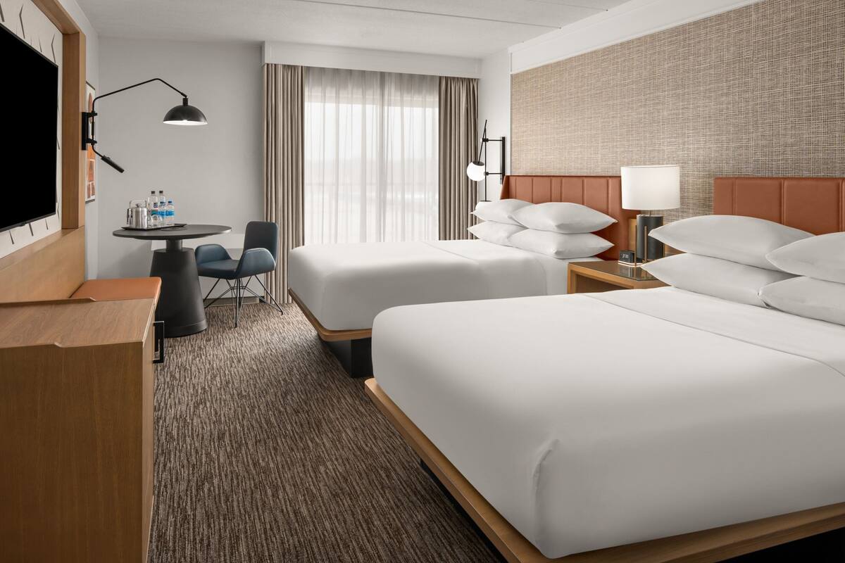 A hotel room with two beds, a desk, a chair, and a television.