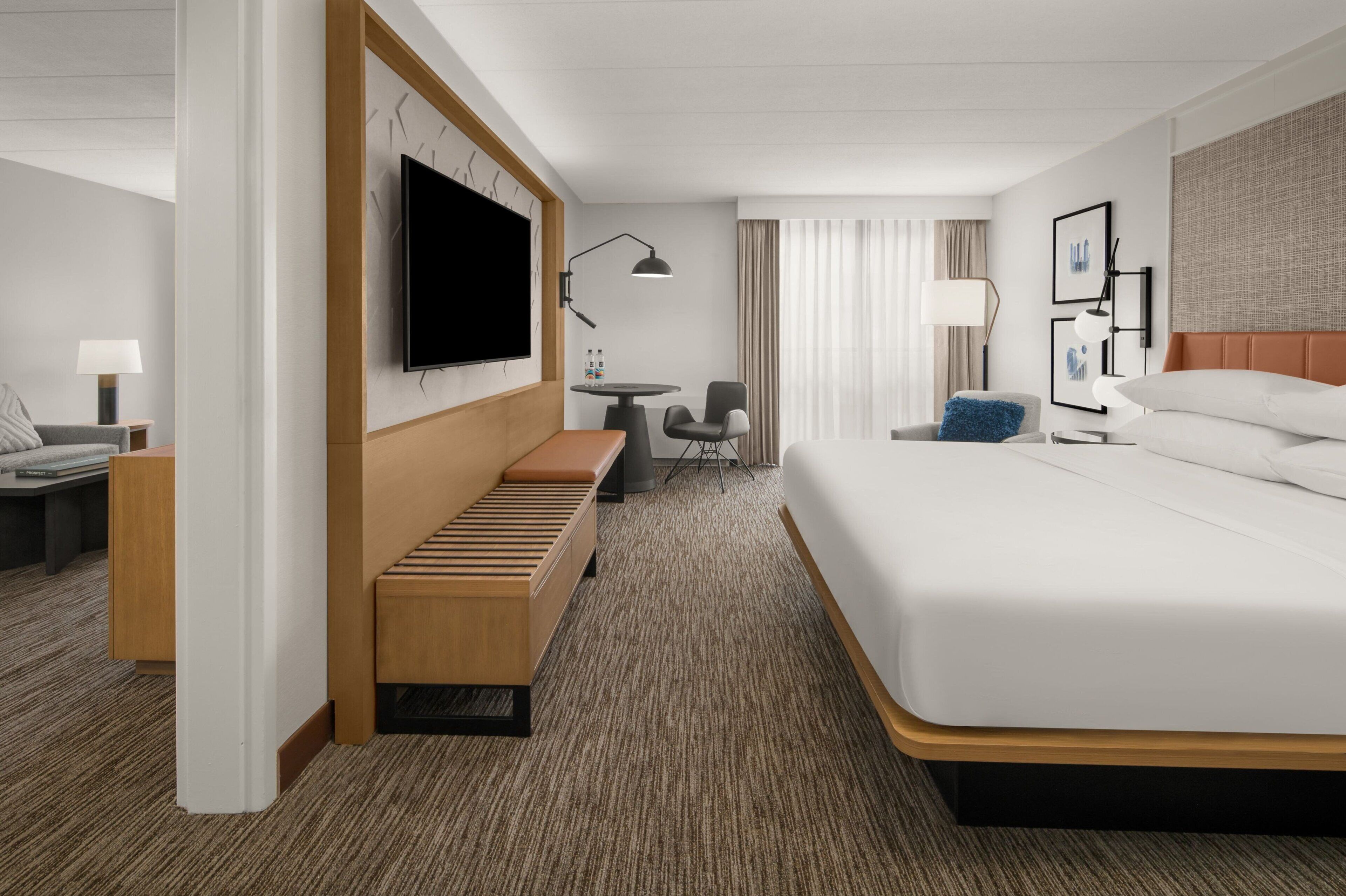 Een hotelkamer met een groot bed, een houten bankje, een bureau met stoel, een flatscreen-televisie en een kleine tafel met lamp.