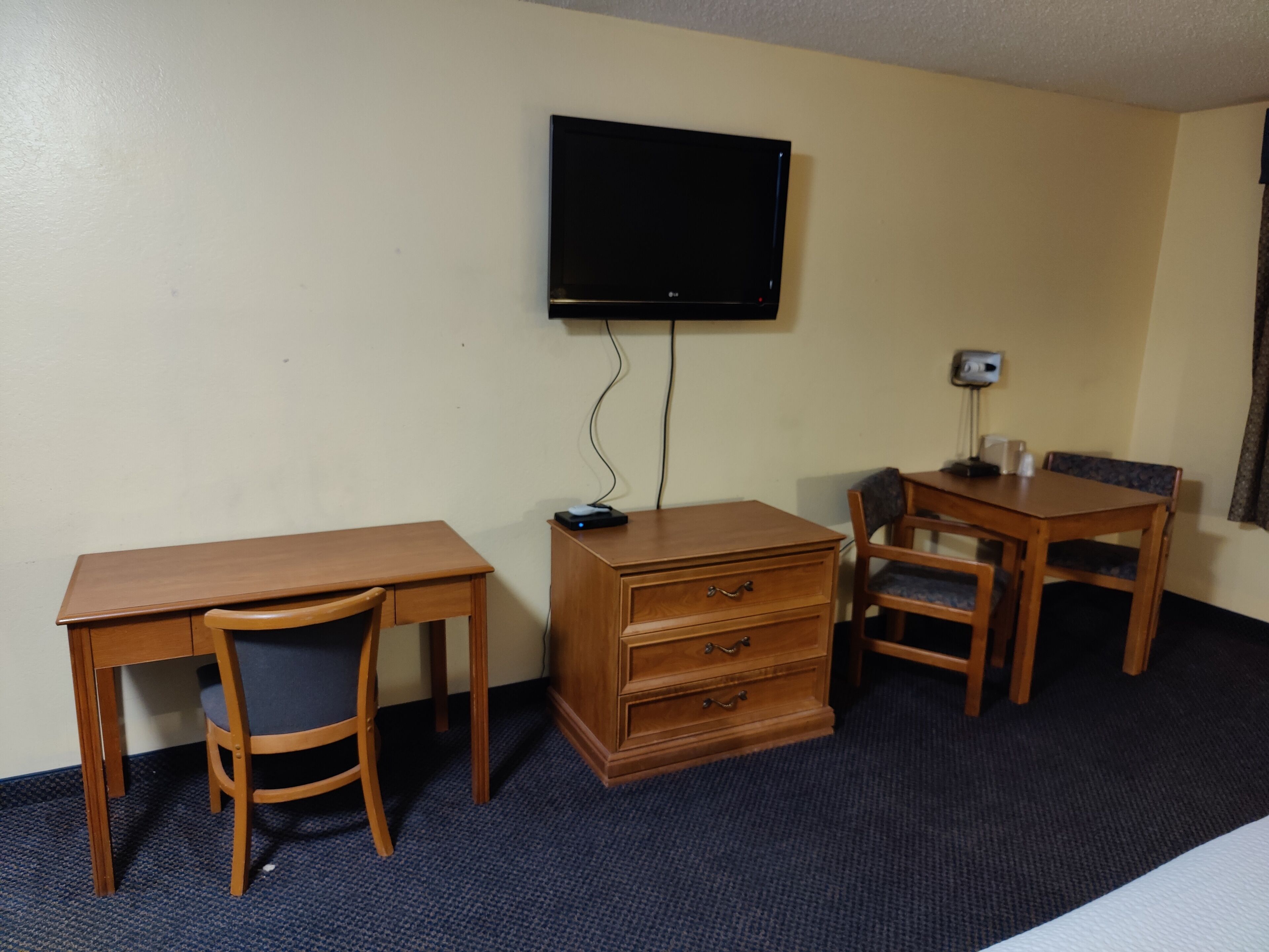 Habitación de hotel con un escritorio de madera, una silla, cómoda, televisor montado en la pared y una lámpara de escritorio.