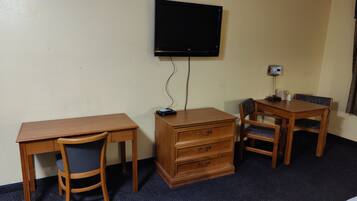 Habitación de hotel con un escritorio de madera, una silla, cómoda, televisor montado en la pared y una lámpara de escritorio.