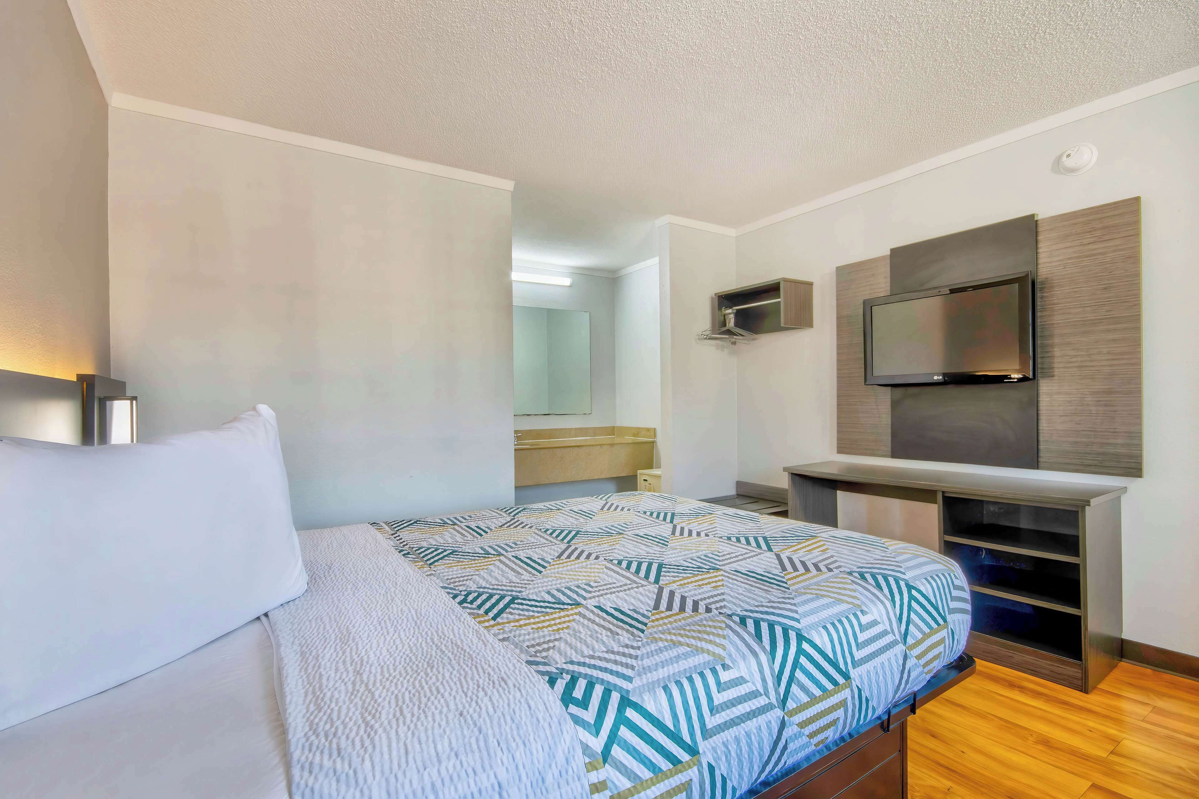Habitación de hotel con cama, televisor montado en la pared y un pequeño escritorio con silla.