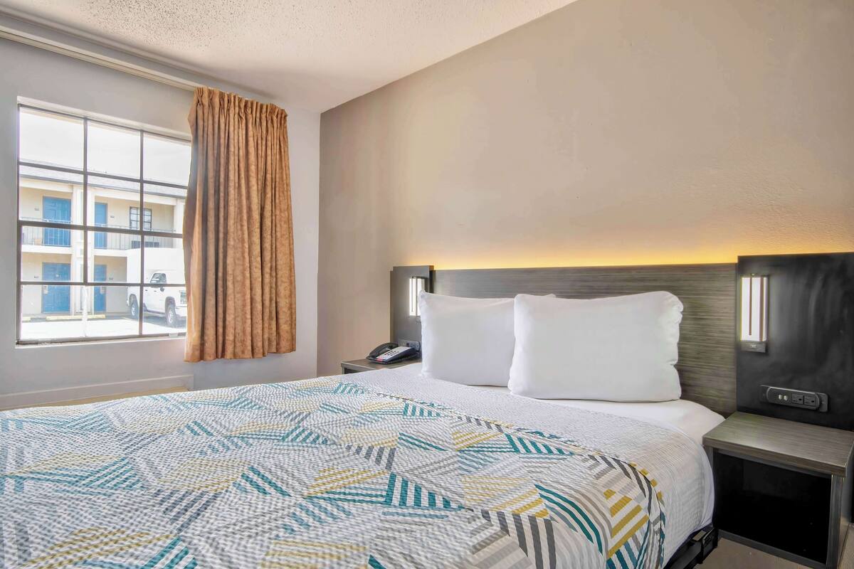 A hotel room with a large bed, a bedside table with a phone, and a window with curtains.