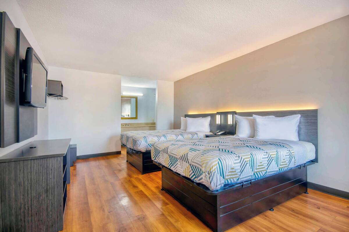 A modern hotel room with two beds, a flat-screen TV, and a wooden floor.