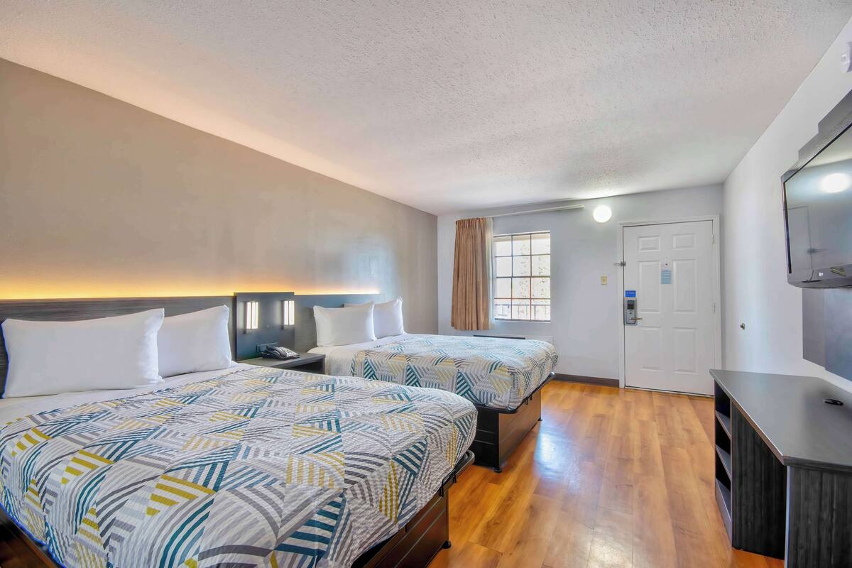 A hotel room with two beds, a TV, a desk, and a window with curtains.