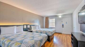 A hotel room with two beds, a TV, a desk, and a window with curtains.