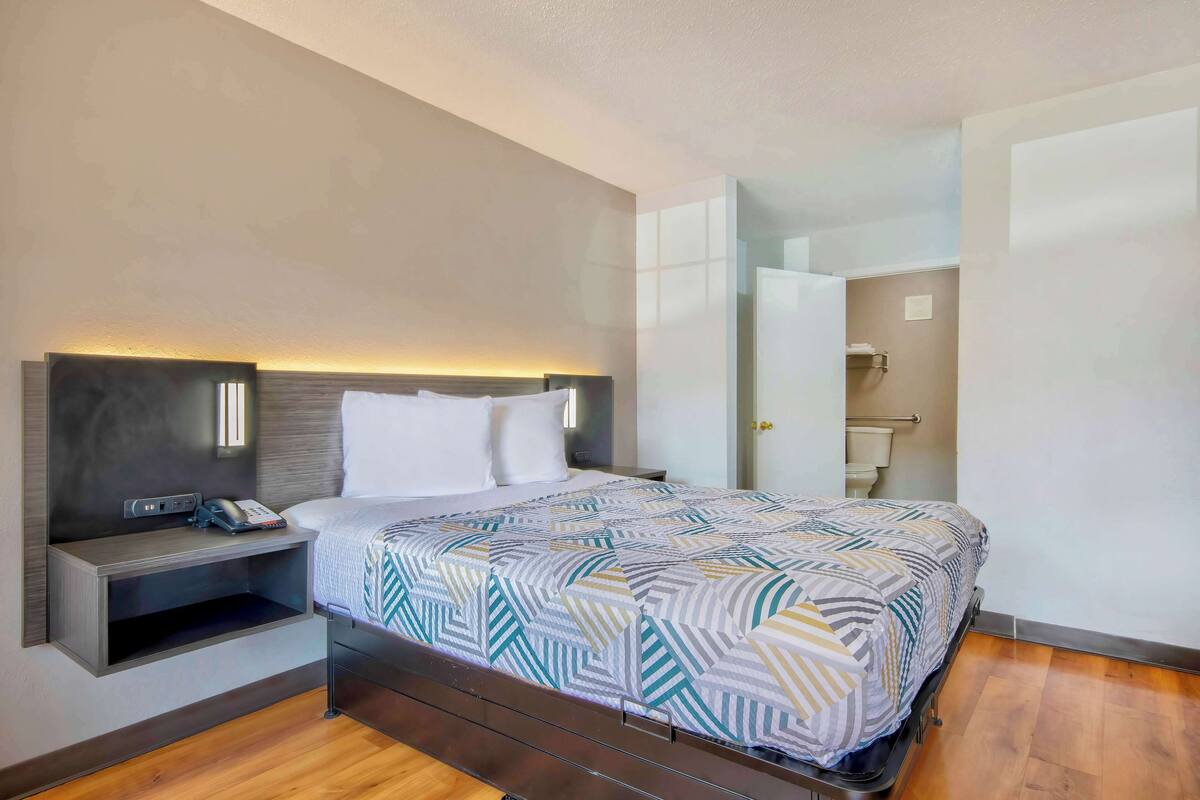A modern hotel room with a bed, bedside table, and a built-in shelf.