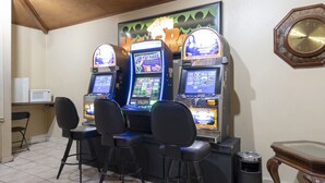 A room with two slot machines, three bar stools, a trash can, a microwave, and a clock on the wall.