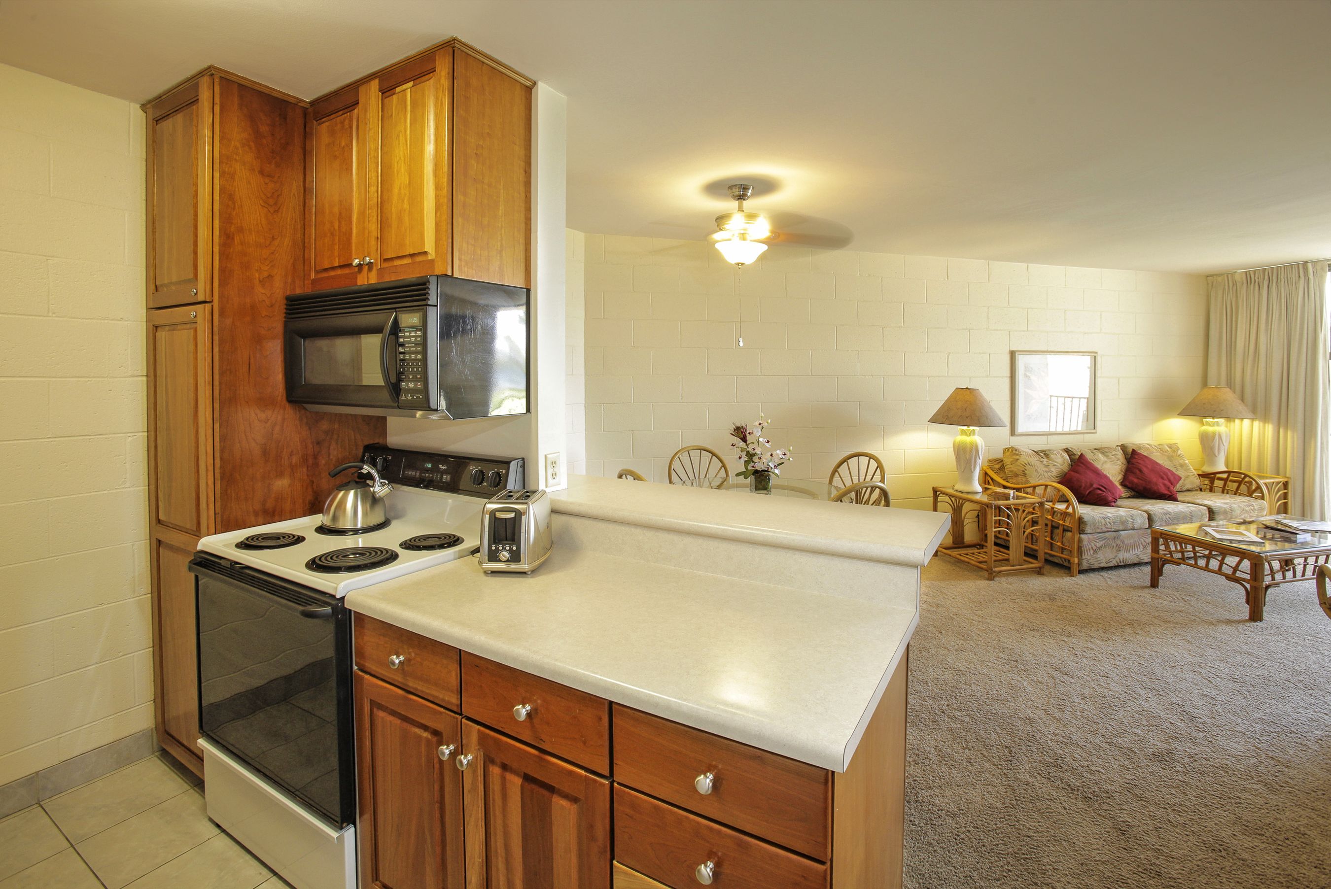 A kitchen with wooden cabinets, a microwave, and a stove. There is a dining area with a table and chairs.