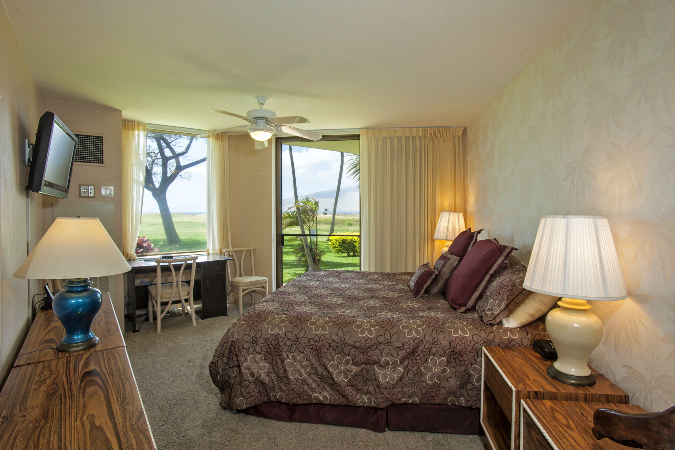 A hotel room with a bed, desk, and chair, a television, and a view of the outdoors.
