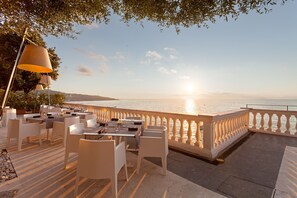 An outdoor dining area with tables and chairs, overlooking a body of water during sunset. - Grand Hotel Cocumella (Sant'Agnello)
