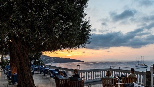 An outdoor seating area with wooden chairs and tables, overlooking a body of water with a sunset in the background. - Grand Hotel Cocumella (Sant'Agnello)