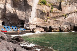 A rocky coastline with a beach area featuring blue lounge chairs and a small boat. - Grand Hotel Cocumella (Sant'Agnello)