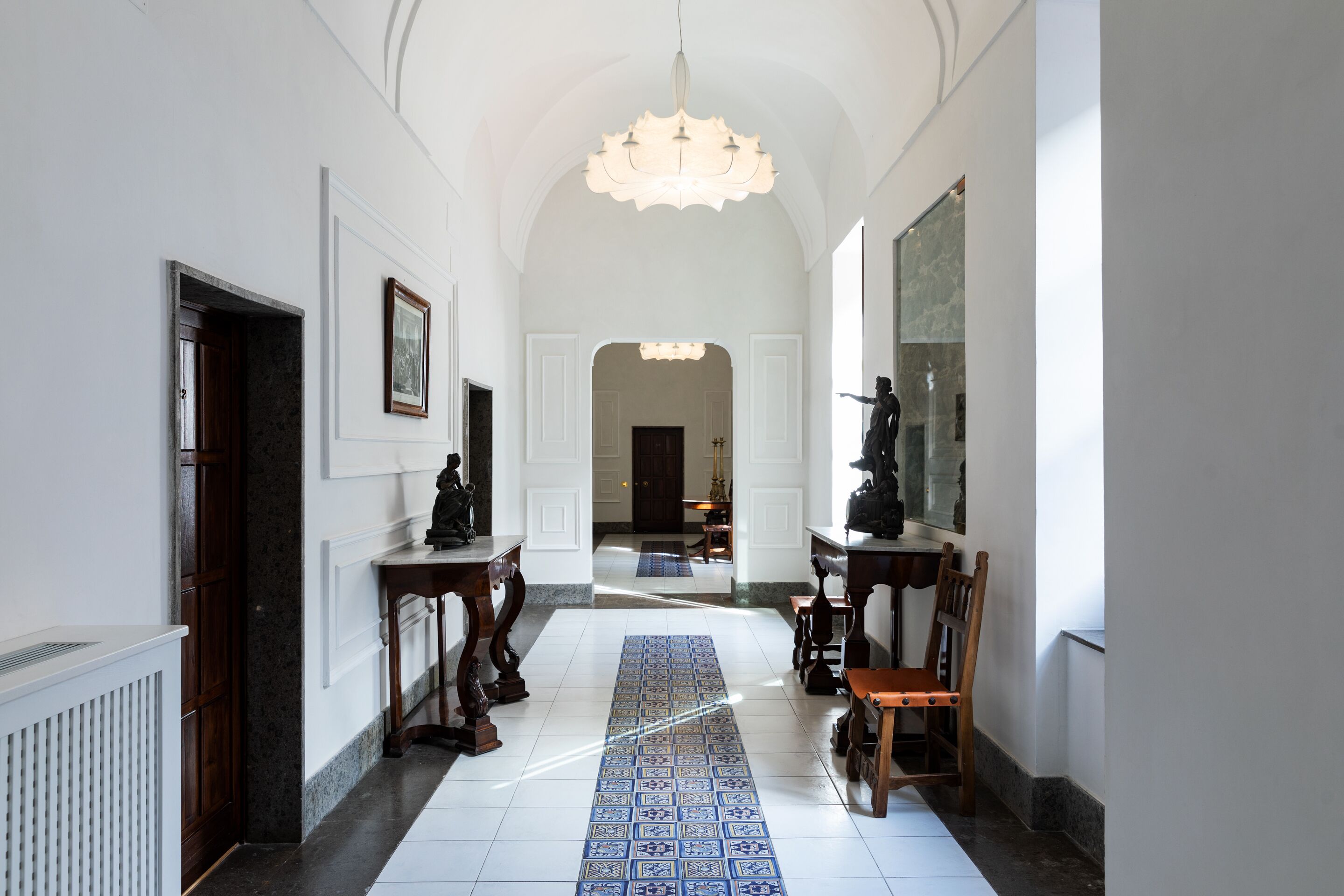 A hallway with a patterned floor, wooden furniture, and a chandelier.