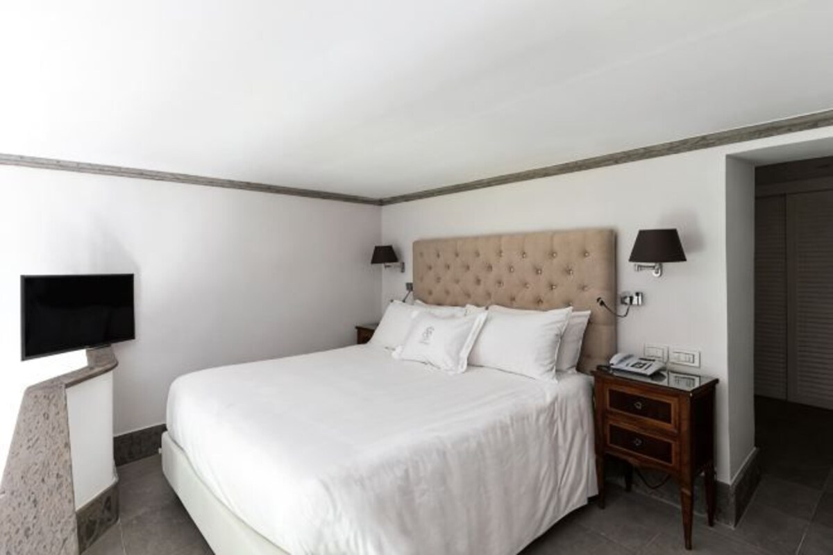 A hotel room with a large bed, bedside lamps, a flat-screen TV, and a telephone on the nightstand.