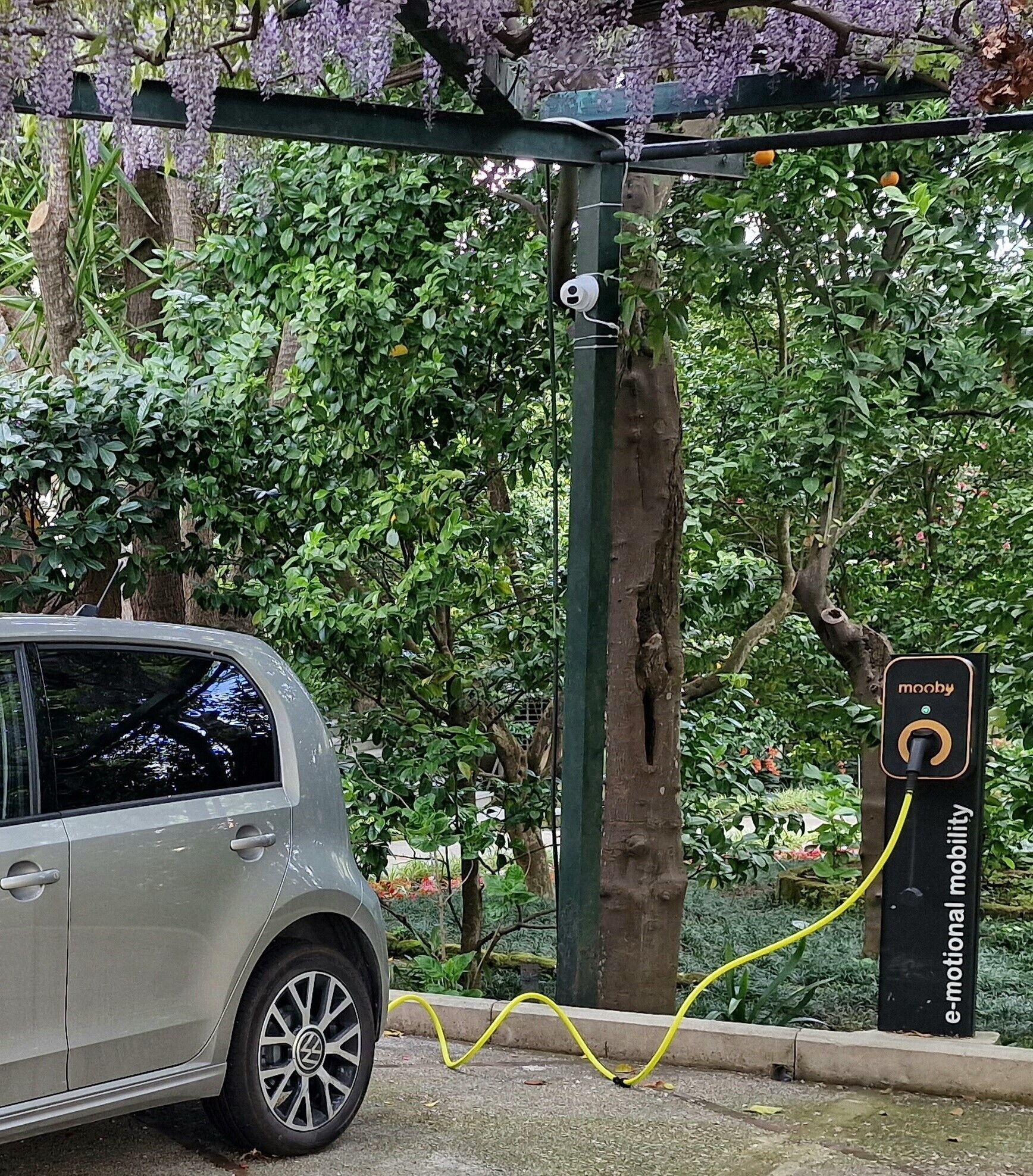 Ein silbernes Auto, geparkt an einer E-Mobilitäts-Ladestation, verbunden mit einem gelben Ladekabel.