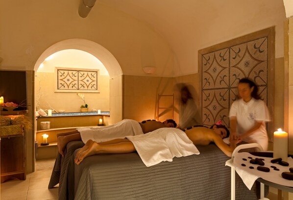 Una stanza spa con due lettini da massaggio, un pannello decorativo a parete e candele.