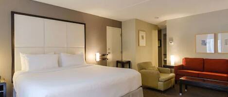 A hotel room with a large bed, a sofa, a chair, and a small table.