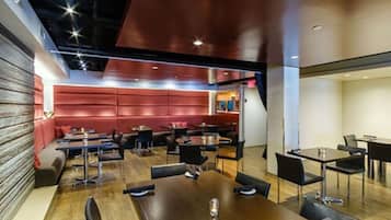 Un restaurante moderno con mesas de madera y sillas negras, un área de estar con cojines rojos y un diseño de techo contemporáneo.