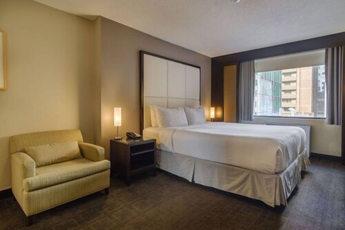 A hotel room with a large bed, a sofa, a nightstand, and a window with curtains.
