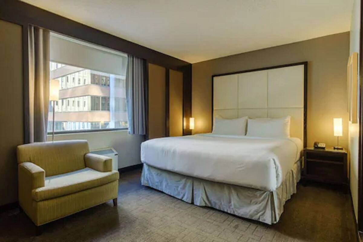 A hotel room with a large bed, a chair, a nightstand, and a window with curtains.