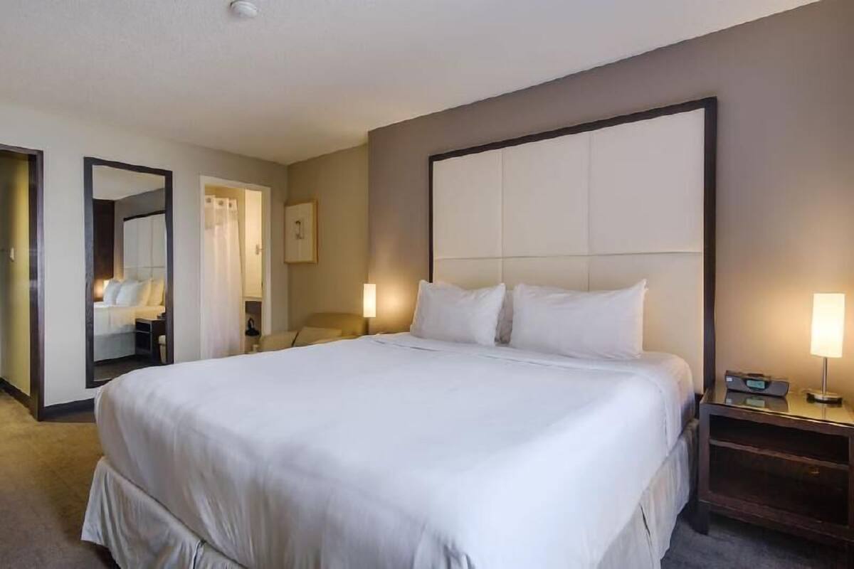 A hotel room with a large bed, a bedside table with a lamp, a mirror, and a framed picture on the wall.