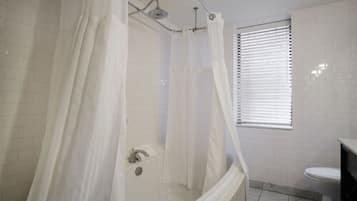 A bathroom with a shower, toilet, and a window with blinds.