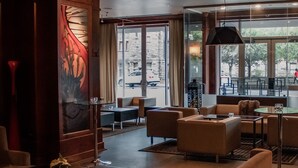 Et moderne loungeområde med sofaer, borde og et stort vindue med udsigt til gaden.