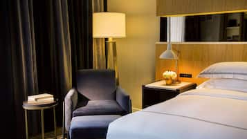 Ein Hotelzimmer mit einem Bett, einem Sessel, einem kleinen Tisch mit einer Lampe und einem Nachttisch mit Lampe und Blumen.