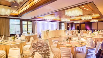 Un salón de banquetes con mesas redondas, manteles blancos y sillas con fundas blancas.