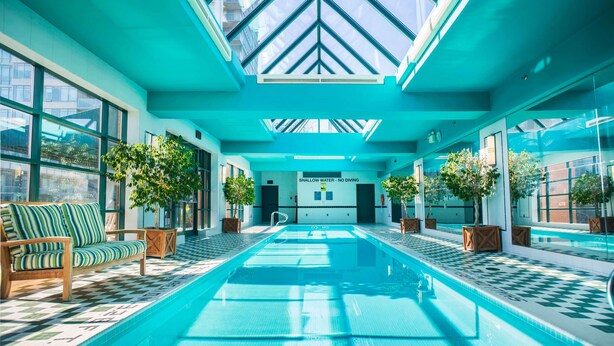 En indendørs swimmingpool med et ternet gulv, træbænke og krukkeplanter.