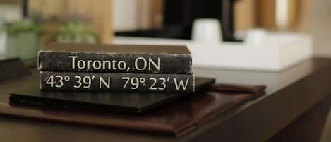 Balcão de recepção de hotel com uma placa preta exibindo as coordenadas de Toronto, Ontário.